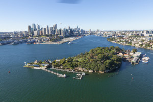 Aerial view of Goat Island – Me-mel in the foreground with the city of Sydney on the skyline behind. The blue water of Sydney Harbour surrounds the island.