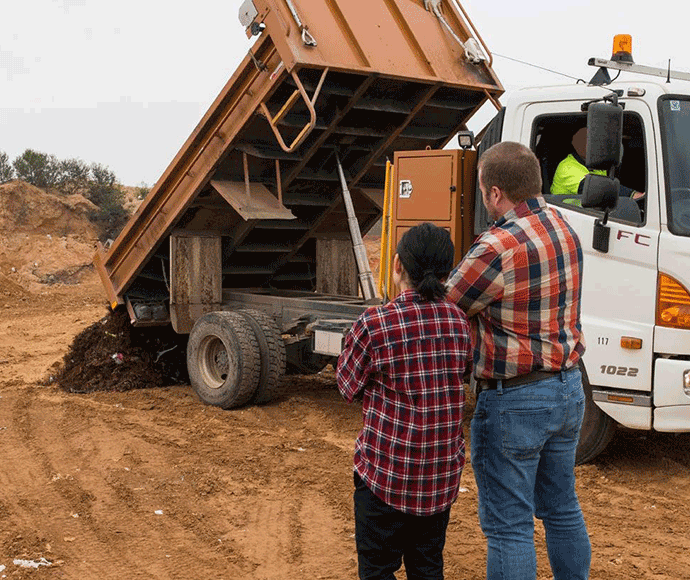 Two people watching soil being tipped from a truck