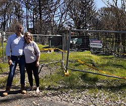 A couple outside a fenced off fire damanged property which has a Danger Asbestos sign