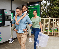 man carrying a young girl on his back and woman leaving a return and earn machine